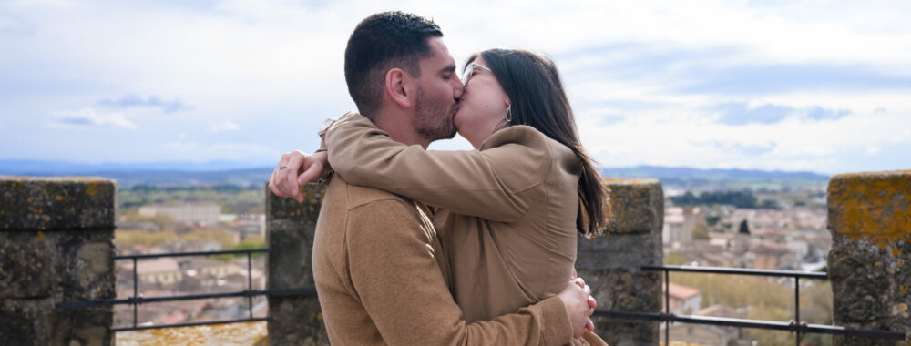 photo de couple qui s'embrasse, en haut du clocher de l'église Saint Vincent à Carcassonne, centre-ville, Bastide Saint Louis. il y a un beau ciel bleu et une vue sur les Pyrénées.