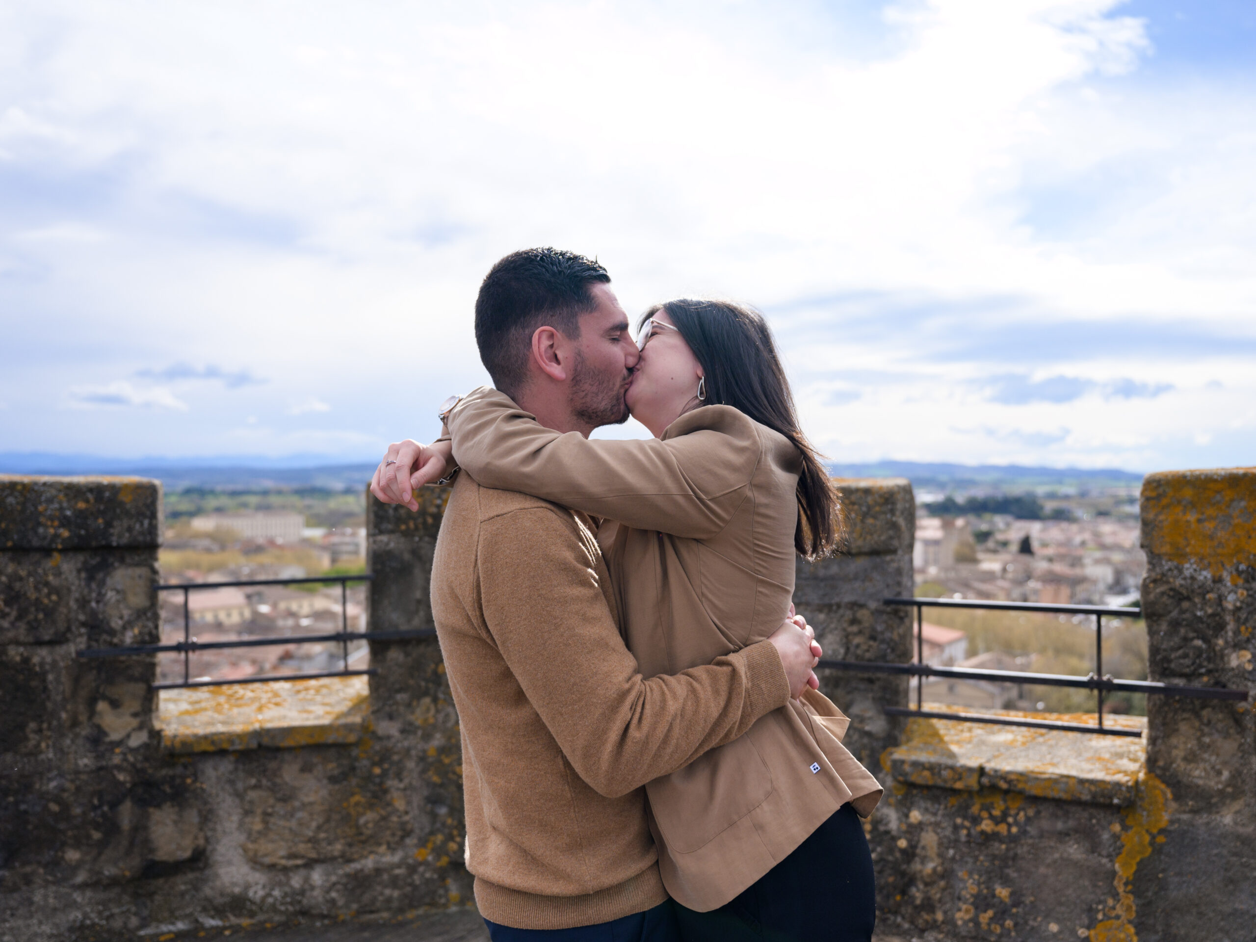 photo de couple qui s'embrasse, en haut du clocher de l'église Saint Vincent à Carcassonne, centre-ville, Bastide Saint Louis. il y a un beau ciel bleu et une vue sur les Pyrénées.