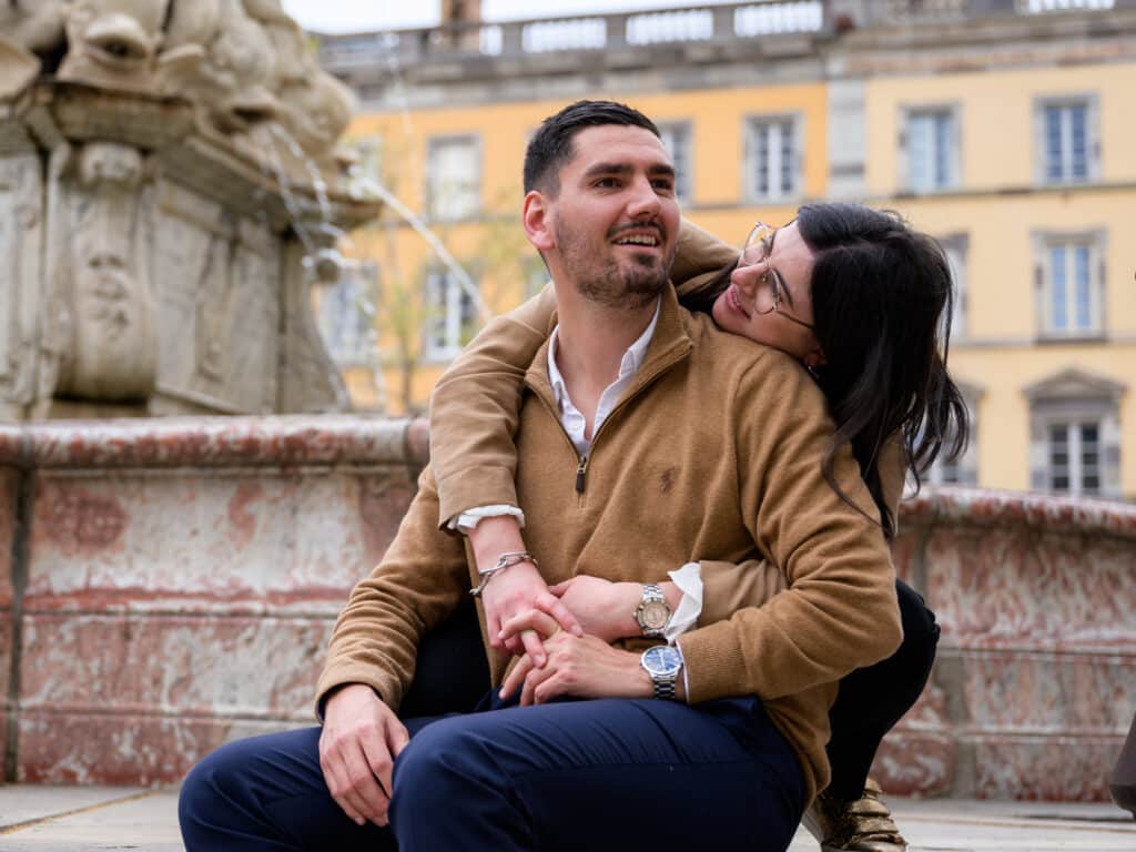 séance photo de couple sur la fontaine Neptune, Place carnot à Carcassonne. Ils sont souriants, enlacés, mains dans les mains.