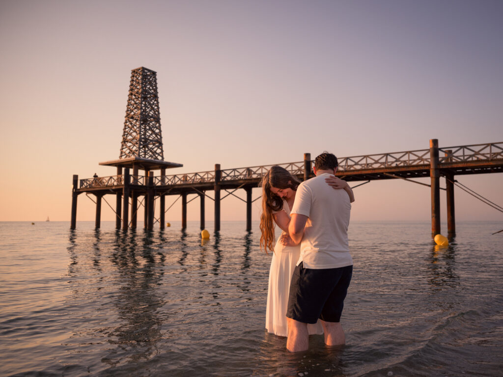 Photos de fiançailles au bord de la mer : la séance de Claire & Luc à Leucate. Séance engagement au lever de soleil au ponton de Leucate. Robe : Aym studio. Bague de fiançailles : Deloison Paris.